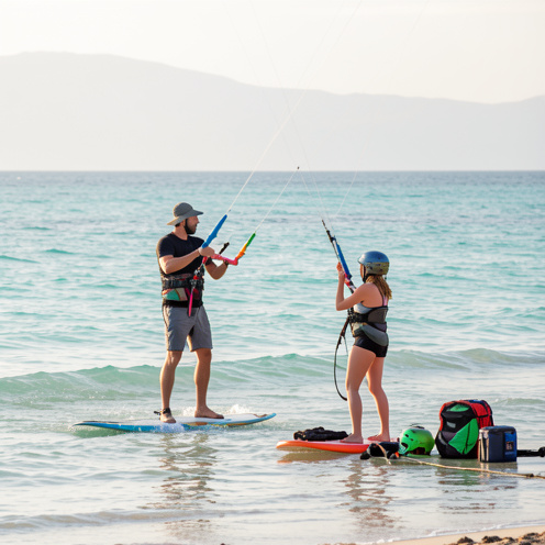 Un instructeur et une débutante apprennent à maîtriser une aile de kitesurf sur une plage peu profonde, avec le matériel et les équipements de sécurité disposés à proximité.
