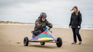 Un homme débutant en char à voile, équipé d’un casque et de vêtements de protection, apprend à piloter sur une vaste plage tandis qu’une instructrice l’accompagne.