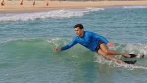 Jeune homme débutant en bodysurf glissant en sécurité sur une petite vague près d’une plage, dans une eau turquoise et calme.