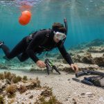 Un homme débutant en pêche sous-marine explore calmement un récif rocheux avec une combinaison, un masque, des palmes et une bouée de sécurité.