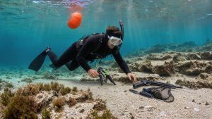 Un homme débutant en pêche sous-marine explore calmement un récif rocheux avec une combinaison, un masque, des palmes et une bouée de sécurité.