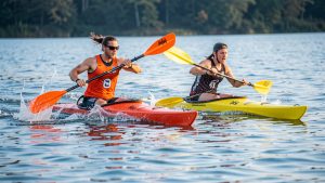 Deux athlètes, un homme et une femme, pagaient avec énergie dans des kayaks colorés sur un lac, illustrant la puissance, l’agilité et l’endurance du kayak-polo.