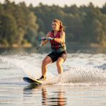 Une femme sportive pratique le ski nautique sur un lac calme, en travaillant son équilibre et sa stabilité corporelle dans une lumière matinale.